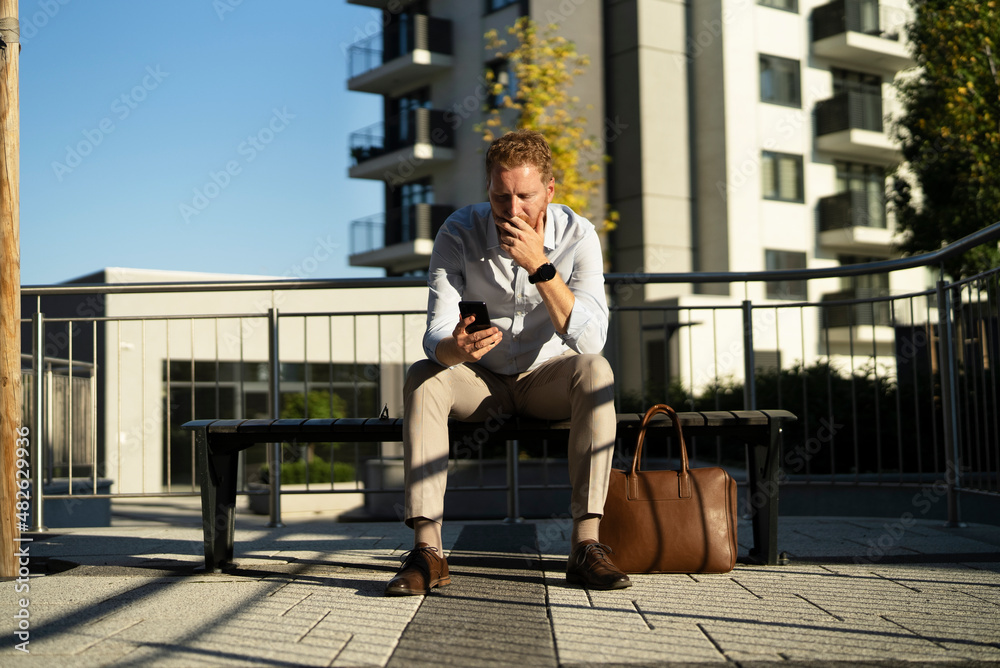 Young stylish businessman sitting on the beanch outdoors. Portrait of handsome man using the phone.. Young stylish businessman sitting on the beanch outdoors. Portrait of handsome man using the phone..