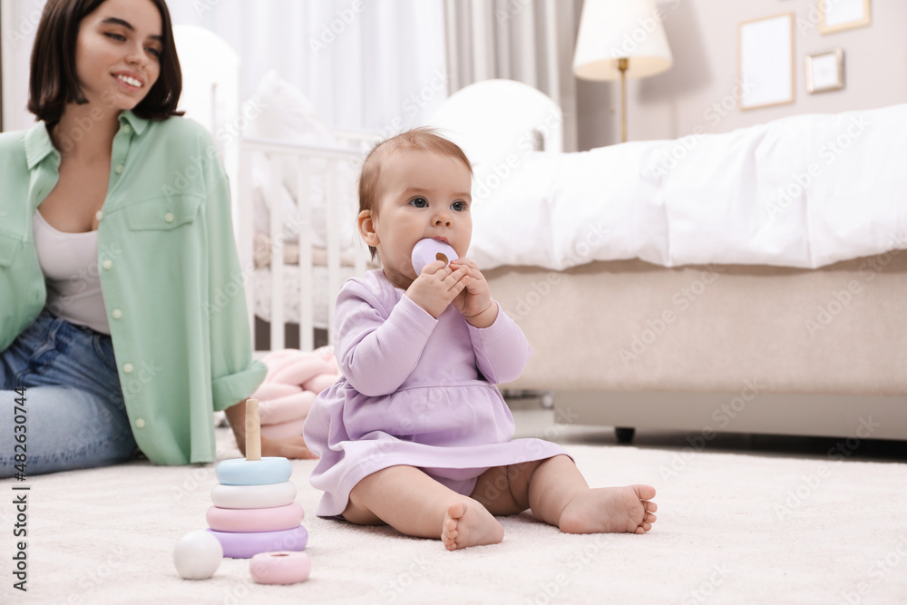 Cute baby girl playing with toy pyramid near mother on floor at home Cute baby girl playing with toy pyramid near mother on floor at home