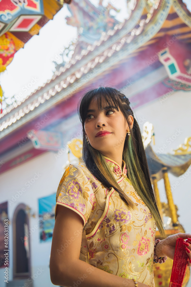 Beautiful Asian woman wearing traditional yellow cheongsam qipao dress standing and looking away in Chinese temple in Chinese new year festival.