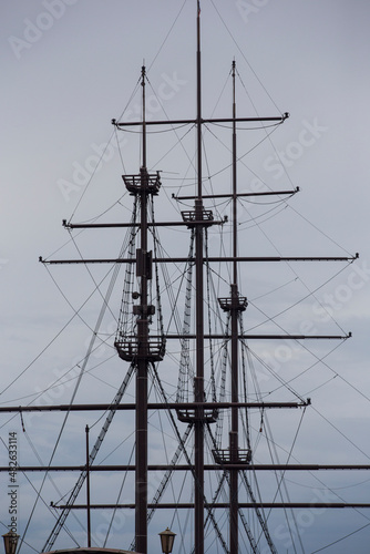 three wooden masts of a Dutch fluyt merchant sailing ship of XVIII century on a grey sky and clouds background close up vertical view