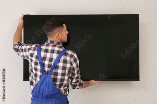 Professional technician installing modern flat screen TV on wall indoors
