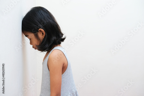 Side view of Asian kid showing sad expression with her head on the wall photo
