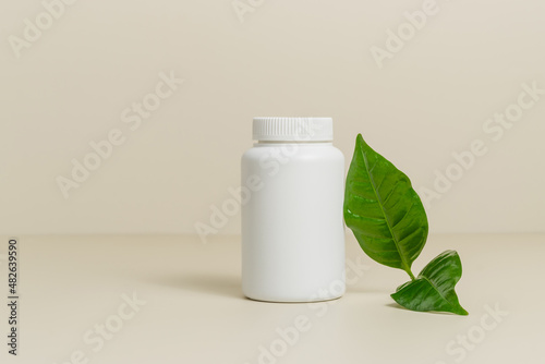 Mockup white medical bottle for pills or vitamins with green leaf, bio supplement, organic vitamins, healthy lifestyle, copy space, beige background