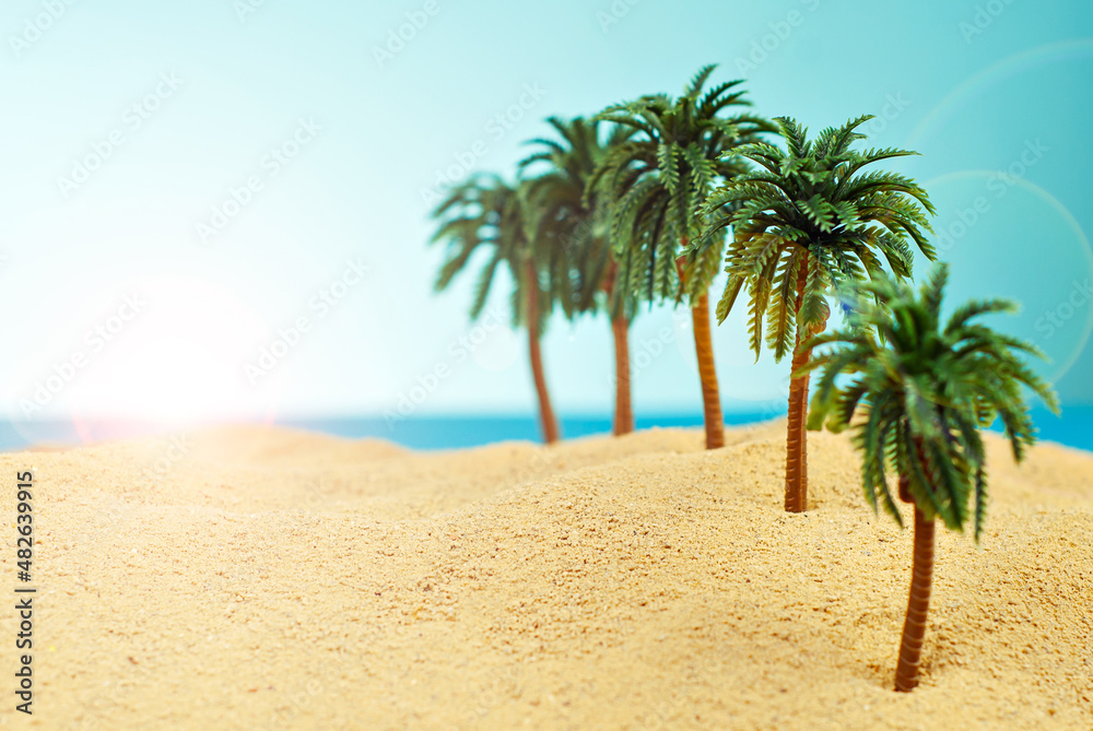 Miniature palm trees on a paradise island. Layout of the beach with palm trees in the sand. Blue sky in the background. The concept of rest and travel.