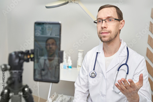 Male doctor talk to patient by phone. Telemedicine content. Tripod hold camera. Blogger therapist. Telehealth media record. Internet clinic speech. Hospital webinar office