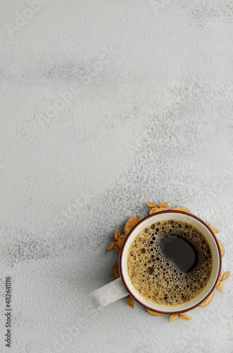 light photo with soft light. White cup with black coffee on a wooden stand for hot, on a gray background, top view with negative space.