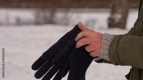 Closeup side view 4k slow motion video footage of two male cold hands of caucasian traveler. Man puts on warm dark blue gloves standing otdoor isolated on snowy winter landscape background photo