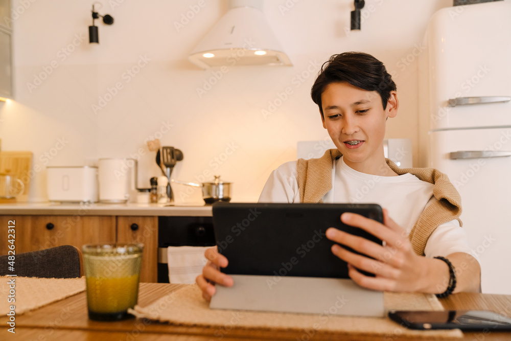 Asian boy using tablet computer while sitting in kitchen Asian boy using tablet computer while sitting in kitchen