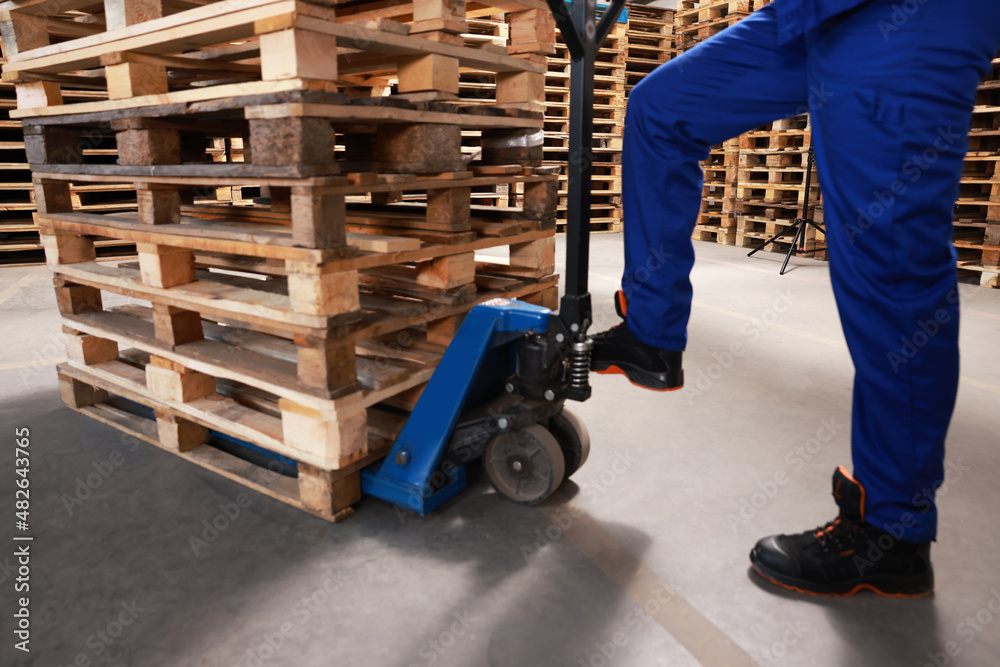 Worker moving wooden pallets with manual forklift in warehouse, closeup