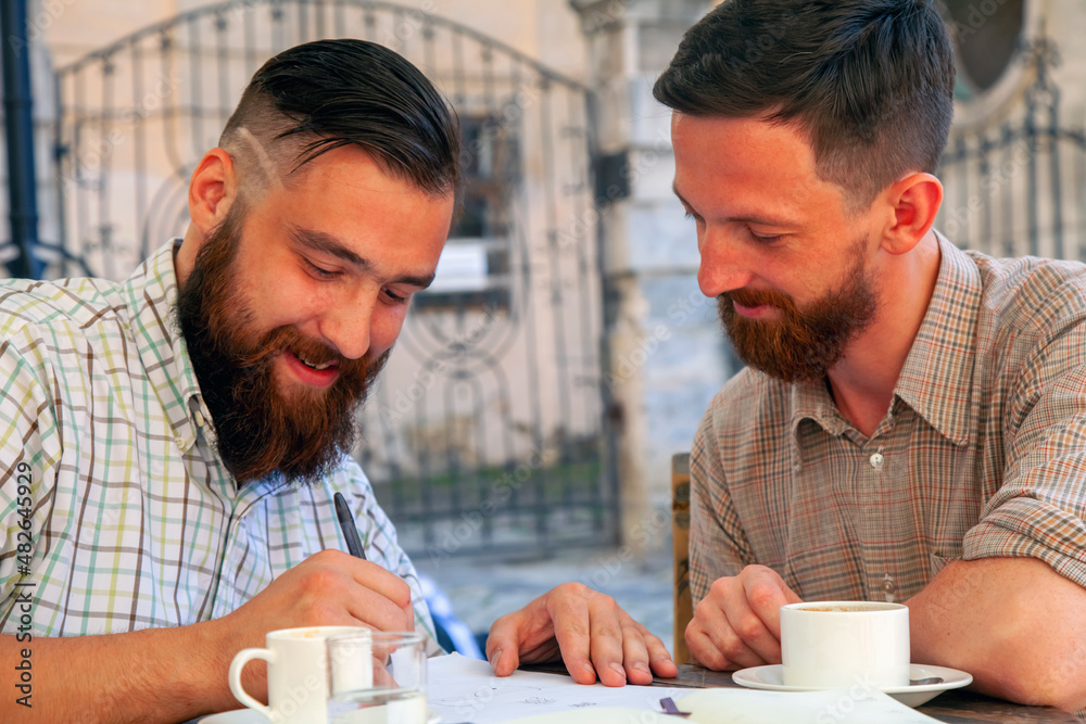Two hipster businessmen working outdoors on the project, laughing and drinking coffee. Concept: happiness, freedom and favorite job.