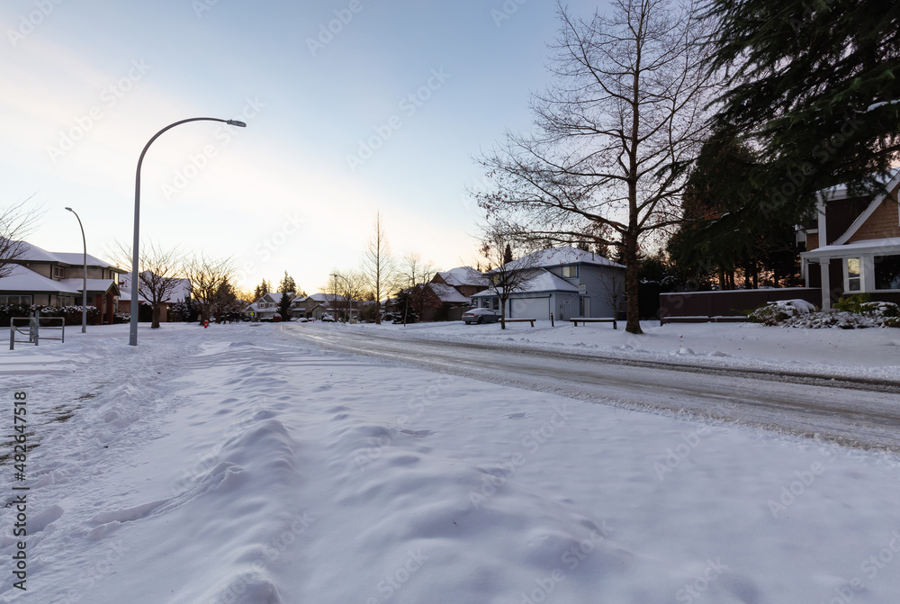 Residential Neighborhood in the Suburbs with White Snow covered road. Sunny Sunrise. Taken in Fraser Heights, Surrey, Vancouver, BC, Canada.