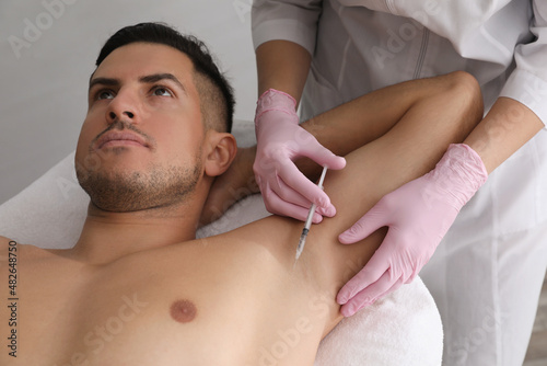 Cosmetologist injecting man's armpit in clinic. Treatment of hyperhidrosis photo