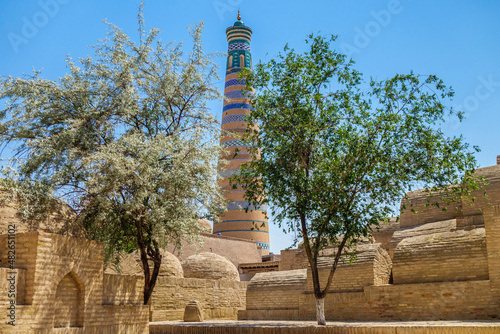Two young trees surrounded by old medieval tombstones. Islam Khodja minaret in the background. Shot in Khiva, Uzbekistan photo