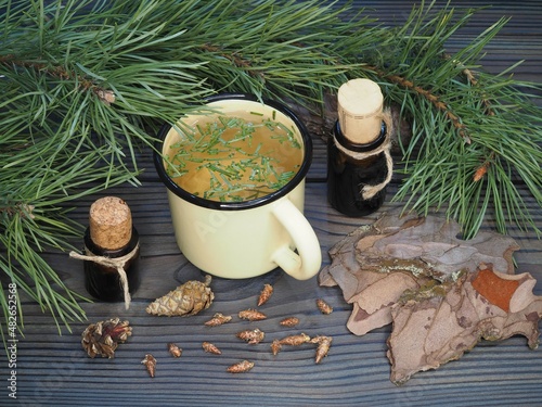 Twigs of pine, cones, pine bark,herbal tea in a mug, oil, tincture extract in bottles on a wooden background, flat layout, top view. Coniferous plant Pinus sylvestris for use in medicine photo