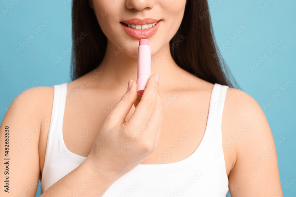Young woman applying lip balm on turquoise background, closeup Young woman applying lip balm on turquoise background, closeup