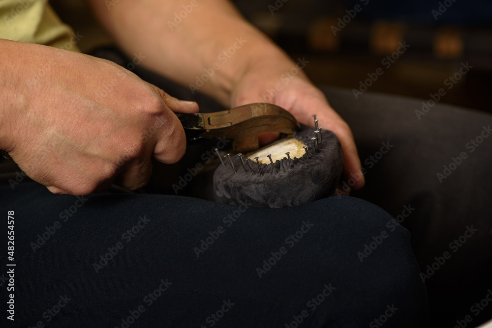 Shoemaker making shoes sitting in workshop. Bootmaker fixing gray suede boot on shoe last with nails and pliers. Closeup.