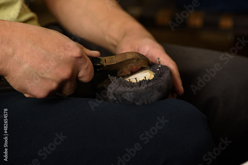 Shoemaker making shoes sitting in workshop. Bootmaker fixing gray suede boot on shoe last with nails and pliers. Closeup. photo