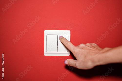 Person activating light switch located on the red wall.