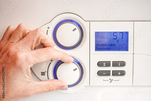 Person activating key for the regulation of a gas boiler located on a wall.