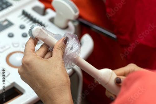 A gynecologist places the ultrasound probe sheath on a trans vaginal ultrasound machine for vaginal examination of a woman using an ultrasound machine. Ultrasound of the pelvic organs. Close-up.  photo