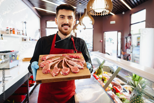 Schilderij op canvas Young butcher holding raw lamb ribs in a butcher shop