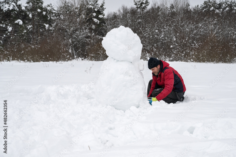 A man makes a snowman in a snow-covered field in the open air. Winter time