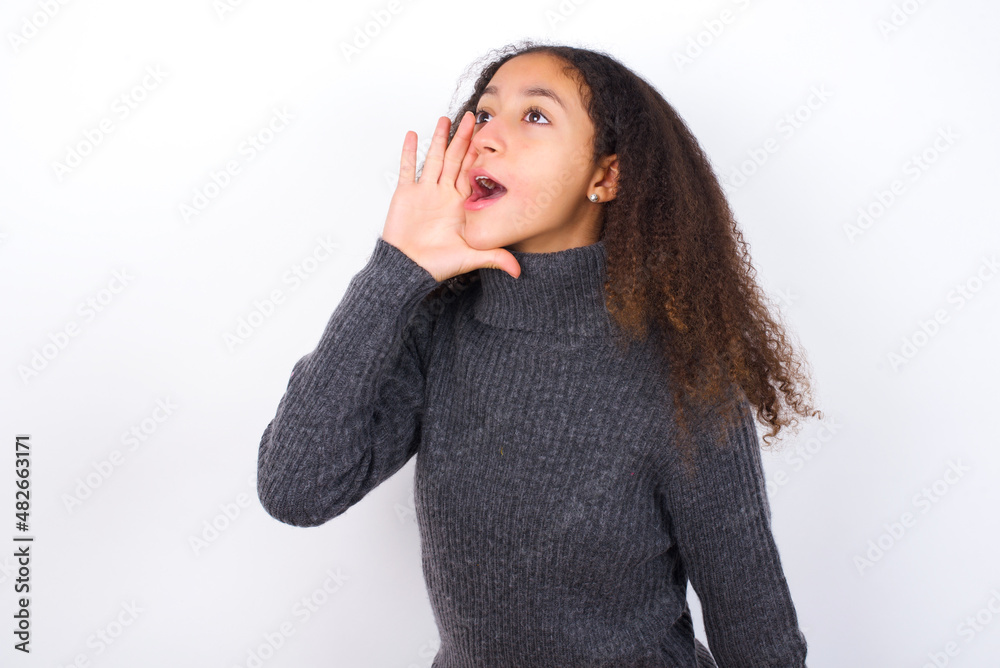 teenager girl wearing grey sweater standing against wite background shouting and screaming loud to side with hand on mouth. Communication concept. teenager girl wearing grey sweater standing against wite background shouting and screaming loud to side with hand on mouth. Communication concept.
