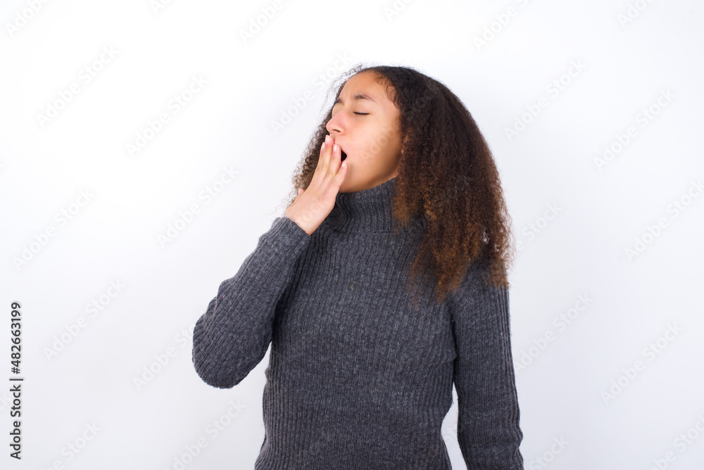 teenager girl wearing grey sweater standing against wite background being tired and yawning after spending all day at work. teenager girl wearing grey sweater standing against wite background being tired and yawning after spending all day at work.
