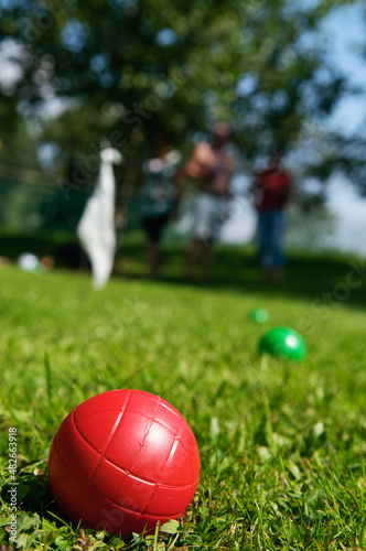Fotografia, Obraz Close-up of red boccia ball lying in grass and people playing in background