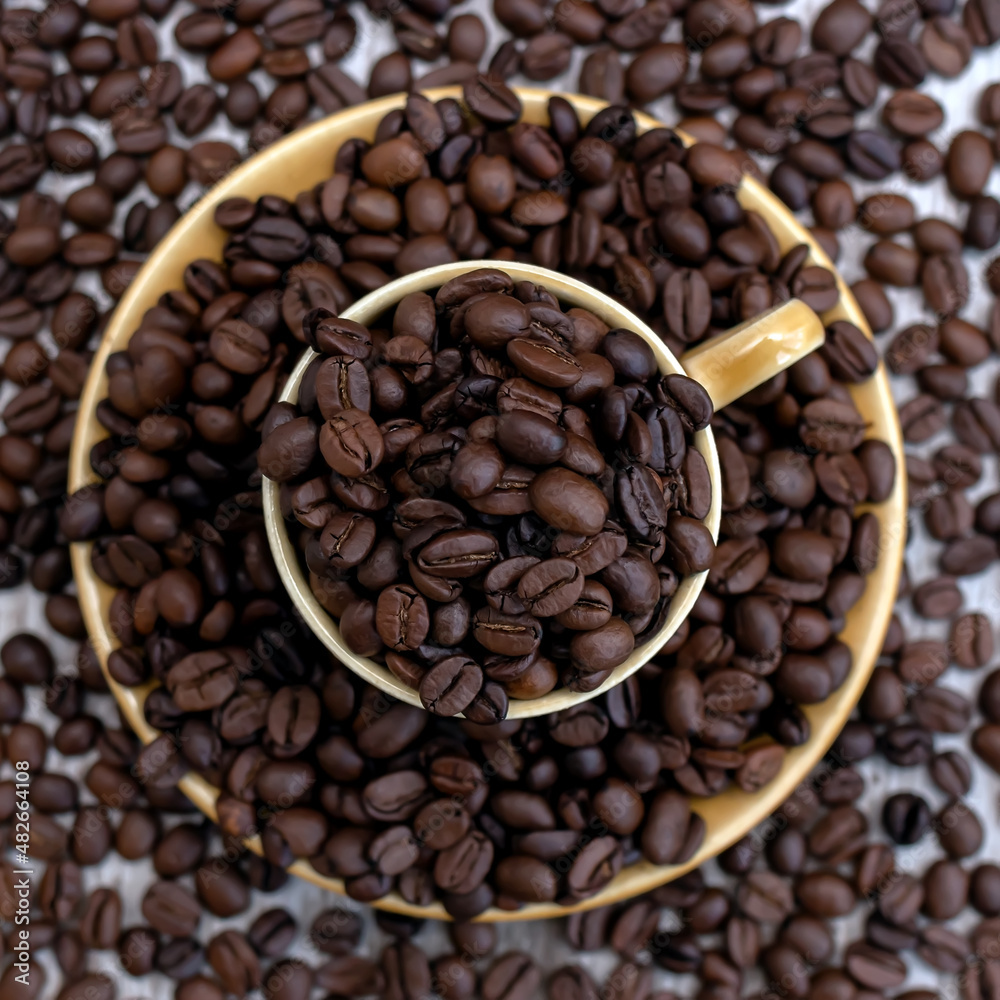 Fototapeta premium A cup filled with coffee beans surrounded by coffee beans. Coffee beans close up. Selective focus. Dried and roasted coffee beans.