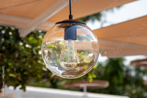 Round transparent beautiful street lighting lantern against the green plant background is in a park in summer