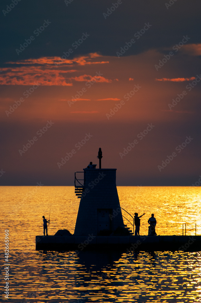 Fototapeta premium People on pier with small lighthouse at sunset