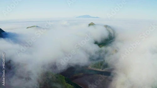 Flight above dense white clouds over dark water with green hills at shoreline