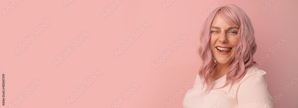 Positive young woman sticking tongue out happy with funny expression posing over bright pink color background