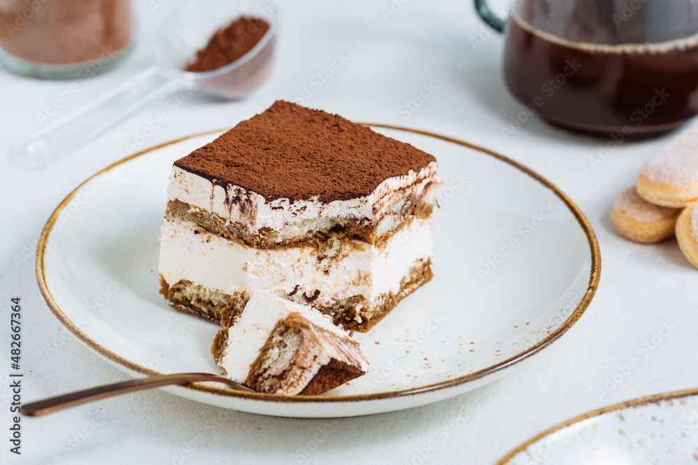 Tiramisu cake dessert served with coffee, biscuit and cocoa as ingredients on a bright white background. One piece of cake Tiramisu cake dessert served with coffee, biscuit and cocoa as ingredients on a bright white background. One piece of cake