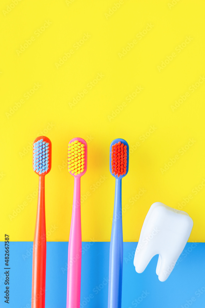 three multi-colored toothbrushes and a figurine of a tooth on a blue-yellow background. dentistry advertising concept..
