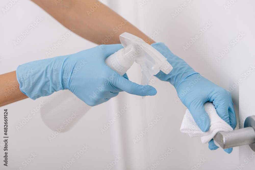 Cleaning black door handle with an antiseptic wet wipe, blue gloves and sanitizer. Woman hand using towel for cleaning. Sanitize surfaces prevention in hospital and public spaces against corona virus Cleaning black door handle with an antiseptic wet wipe, blue gloves and sanitizer. Woman hand using towel for cleaning. Sanitize surfaces prevention in hospital and public spaces against corona virus