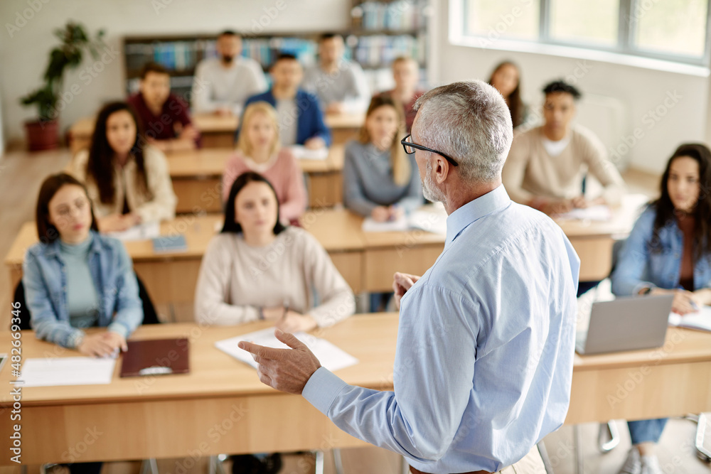 Rear view of mature teacher talking to his student during lecture at university classroom. Rear view of mature teacher talking to his student during lecture at university classroom.