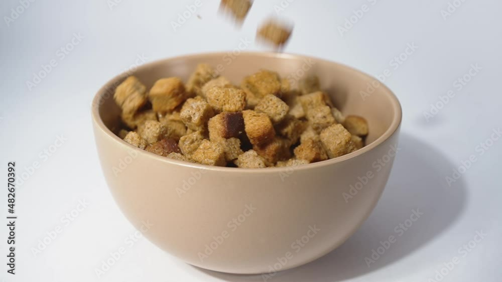 Slow motion. Cubes of fried breadcrumbs fall into the bowl and fill it on a white background. Macro. Slow motion. Cubes of fried breadcrumbs fall into the bowl and fill it on a white background. Macro.