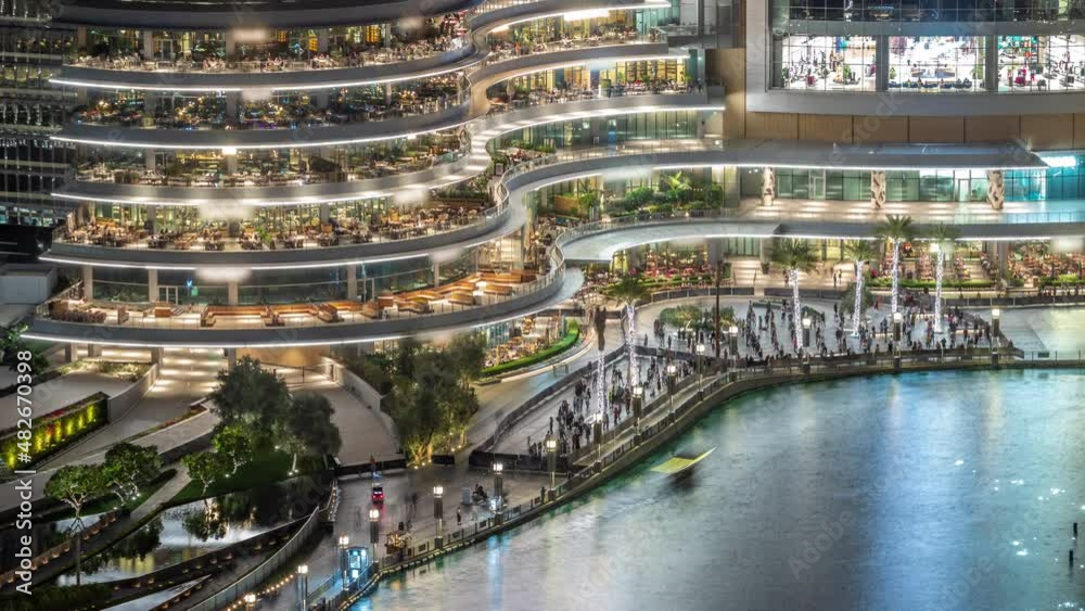 Shopping mall with reataurants near fountain lake in Dubai downtown aerial night timelapse, United Arab Emirates
