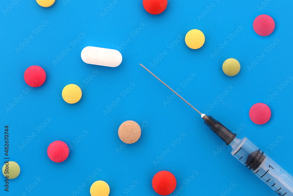 Loose pills and a syringe lie on a blue background.