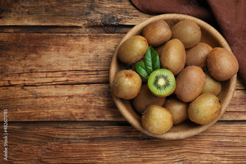 Bowl with cut and whole fresh kiwis on wooden table, flat lay. Space for text