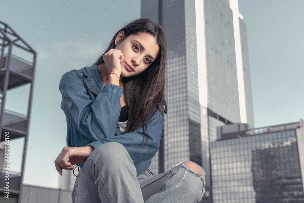 Stylish beautiful casual caucasian hip hop dancer posing sitting in blue jacket, jeans, black top and white tshirt in urban town background. Outdoor city shooting of a model Stylish beautiful casual caucasian hip hop dancer posing sitting in blue jacket, jeans, black top and white tshirt in urban town background. Outdoor city shooting of a model