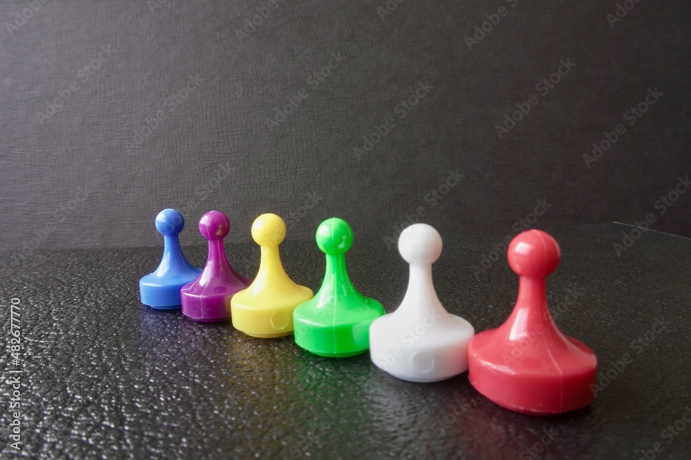 Plastic board game pawns or tokens. Blue, purple, yellow, green, white and red. Plastic board game pawns or tokens. Blue, purple, yellow, green, white and red.