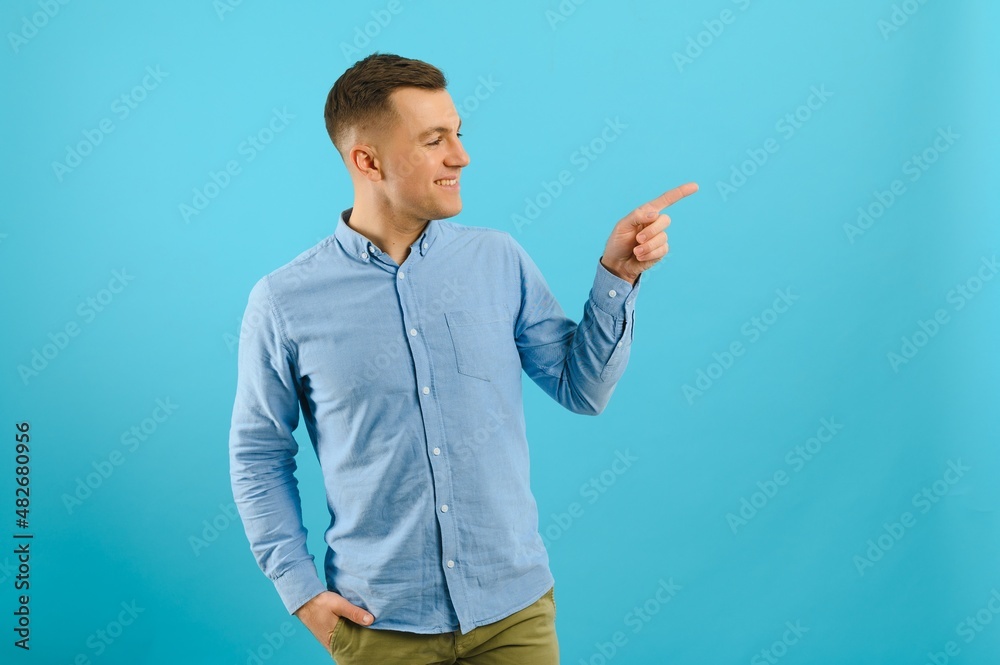 Young handsome man wearing casual t-shirt smiling happy pointing with his thumbs and indicate fingers at copy space over blue background. Young handsome man wearing casual t-shirt smiling happy pointing with his thumbs and indicate fingers at copy space over blue background.