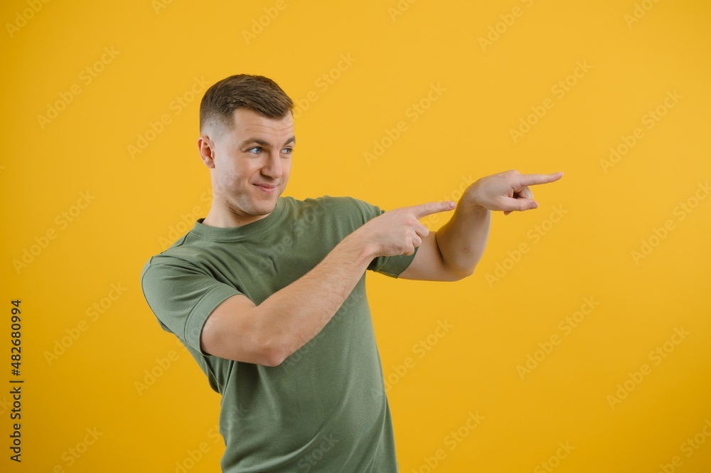 Portrait of a joyful young man pointing fingers away at copy space on his palm isolated over yellow background Portrait of a joyful young man pointing fingers away at copy space on his palm isolated over yellow background