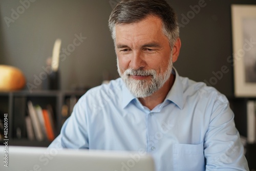 фотографія Portrait of senior man with grey hair working with laptop in office