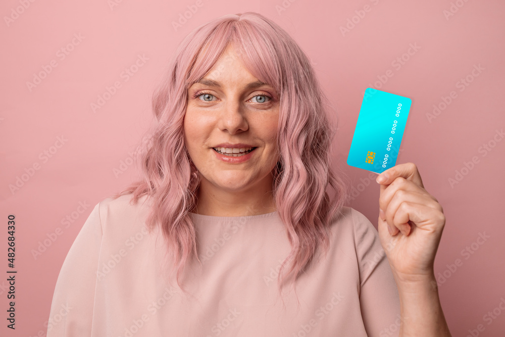 Attractive smiling young woman holds credit card, thinking about shopping isolated on pink studio background. Online shopping. Money finance currency concept Attractive smiling young woman holds credit card, thinking about shopping isolated on pink studio background. Online shopping. Money finance currency concept