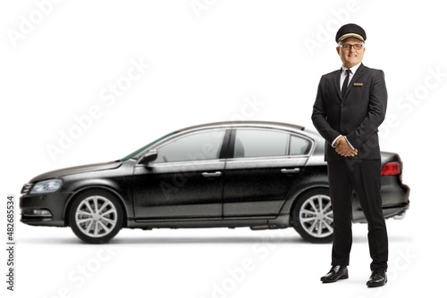 Full length portrait of a chauffeur in a uniform standing in front of a black car © Ljupco Smokovski