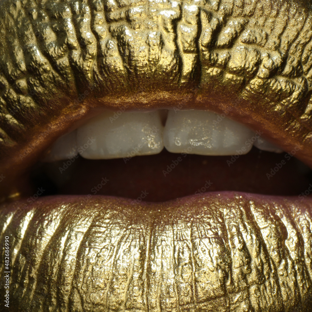 Obraz premium Macro close up gold lips. Gold paint from the mouth. Golden lips on woman mouth with make-up. Sensual and creative design for golden metallic.